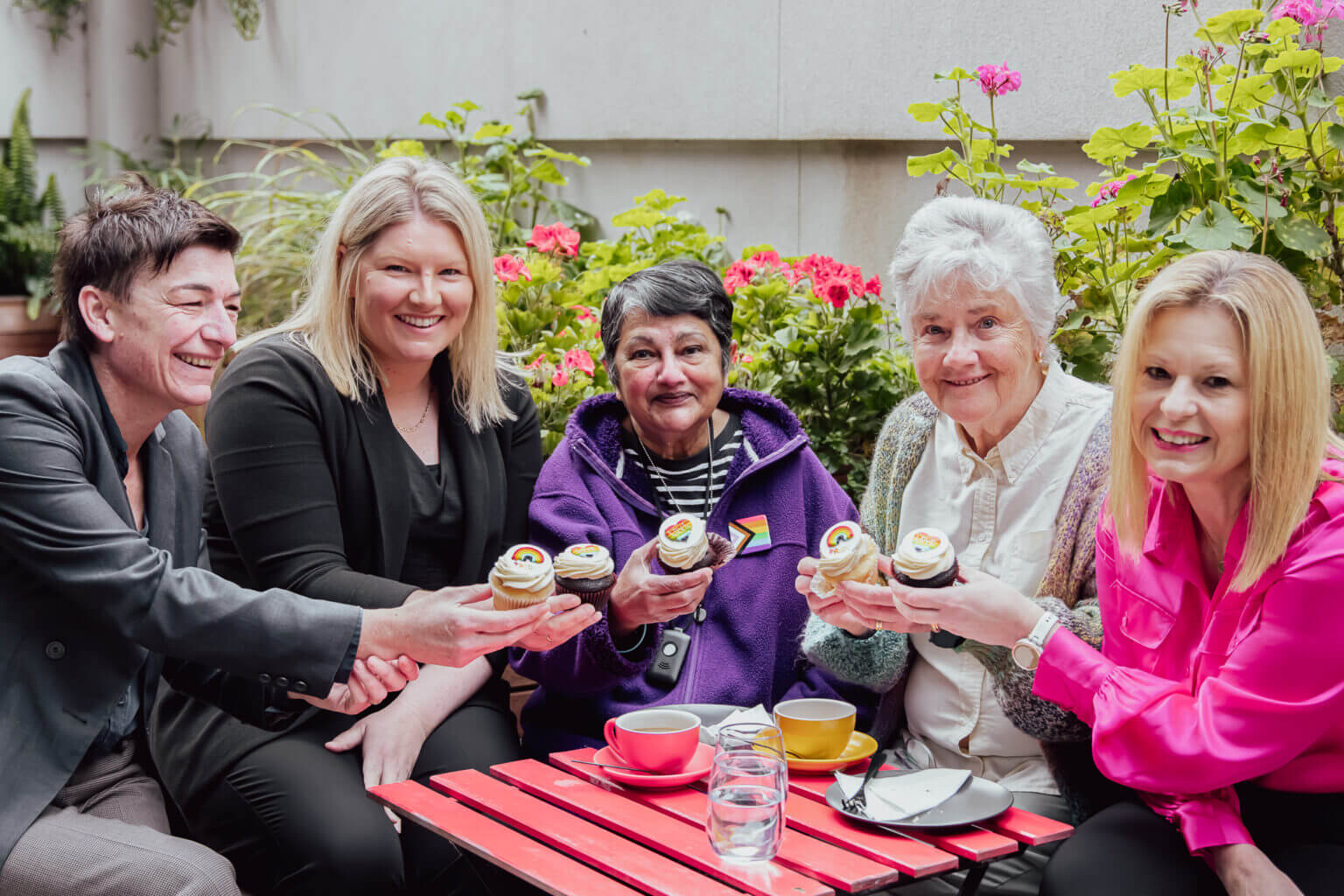 Five people smile and show pride cupcakes to the camera.