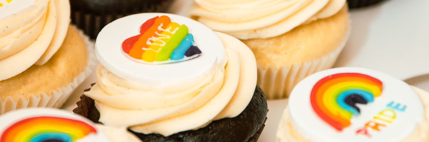 Cupcakes with rainbow designs on top. The focus cupcake reads 'love' over a rainbow heart.